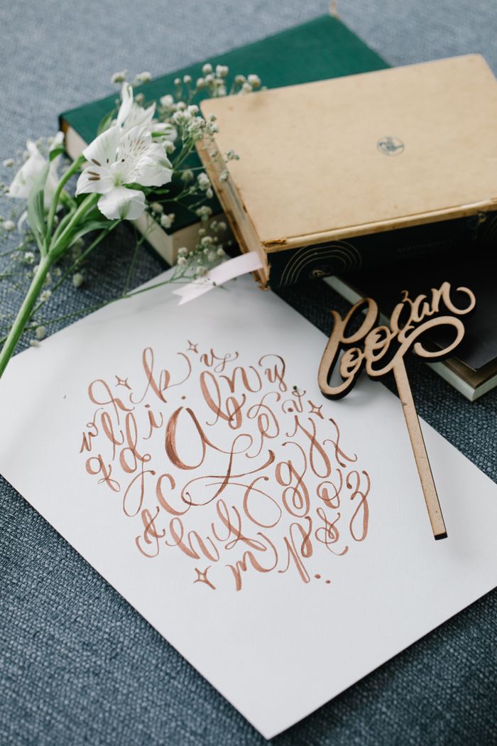 Artistic calligraphy alphabet on paper with books and flowers, perfect for decoration or design inspiration.